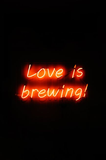 Glowing neon sign displaying 'Love is brewing' on a dark background.