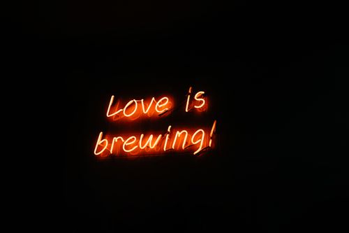 Free Vibrant neon sign displaying the phrase 'Love is brewing!' captured in a dark setting. Stock Photo