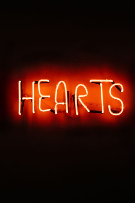 Vibrant neon sign spelling 'Hearts' glowing warmly against a dark background, perfect for modern decor.