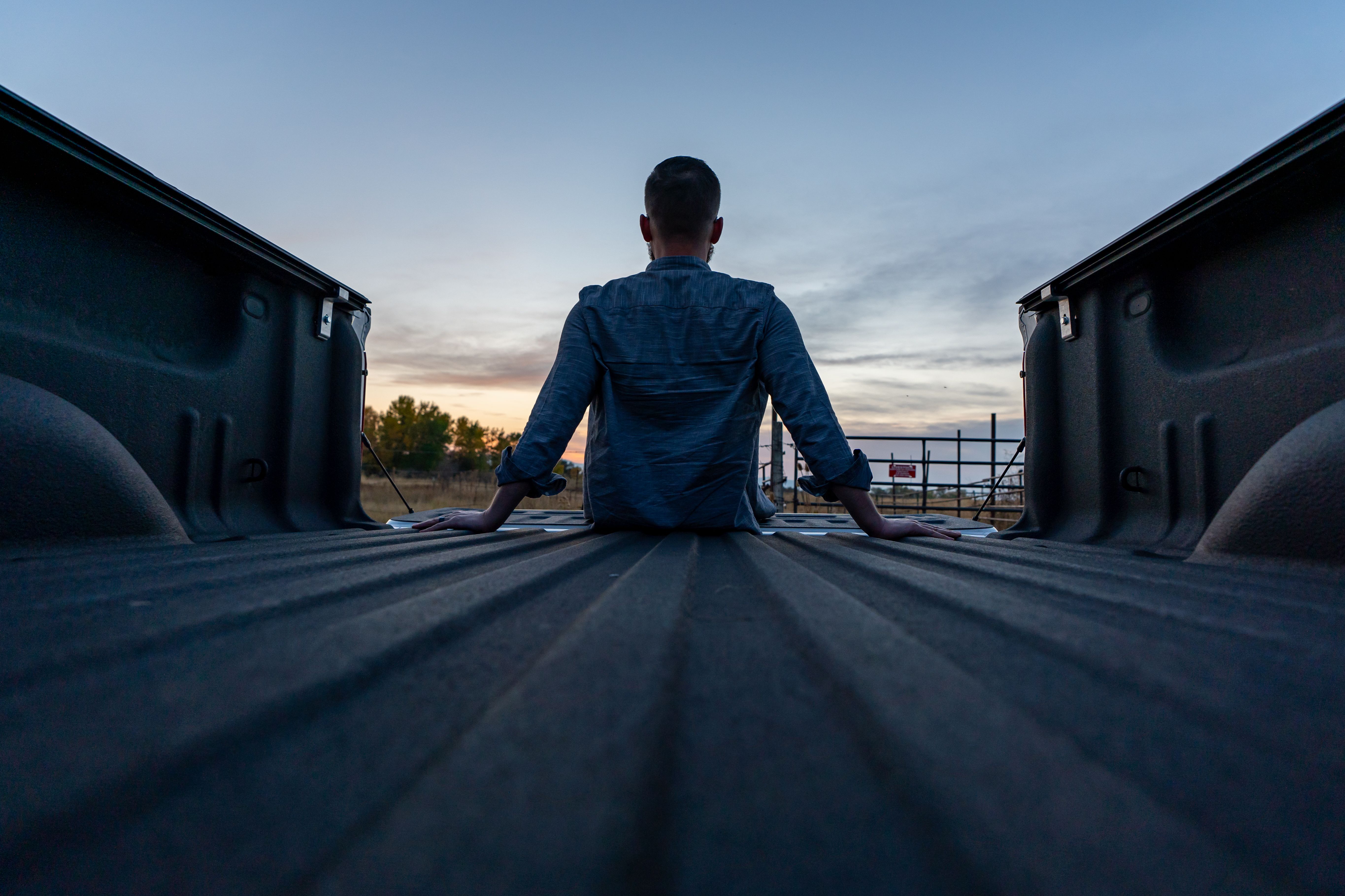 A person sits in the back of a truck watching a serene sunset, capturing a moment of solitude and reflection.