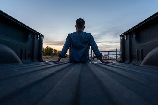 A person sits in the back of a truck watching a serene sunset, capturing a moment of solitude and reflection.