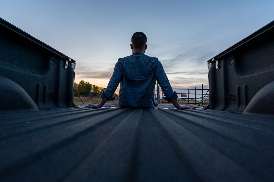 A person sits in the back of a truck watching a serene sunset, capturing a moment of solitude and reflection.
