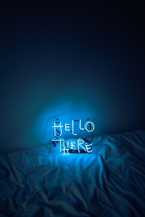 Free Blue neon sign reading 'Hello There' on a bed, creating a moody nighttime ambiance. Stock Photo
