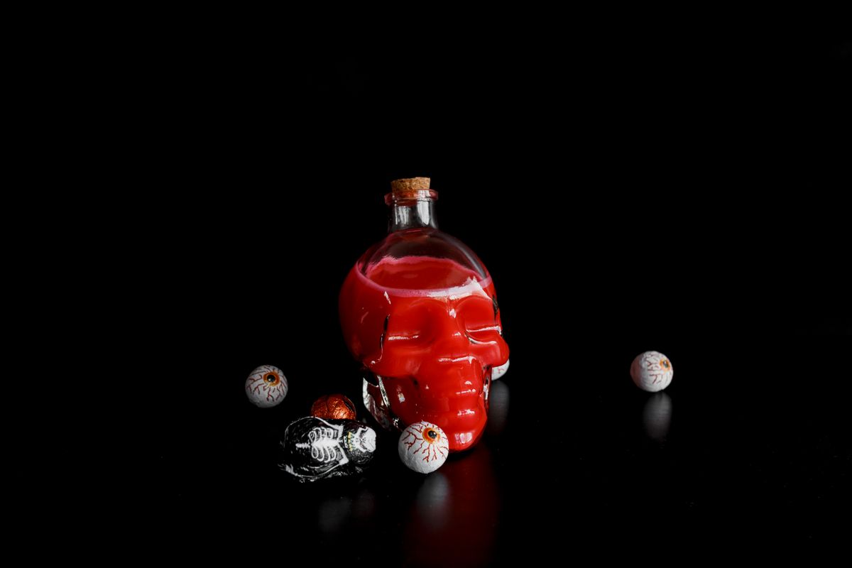 Skull-shaped bottle with red liquid and candy eyeballs on a dark background