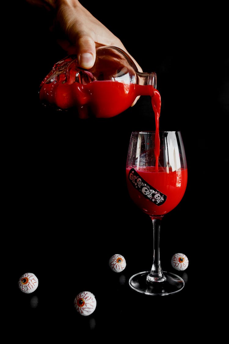 A Person Pouring Red Liquid Into A Glass