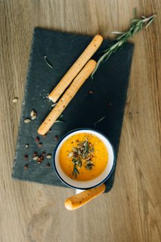 Warm pumpkin soup with breadsticks on slate, garnished with seeds and herbs.