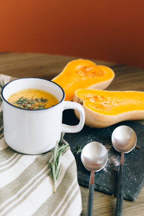 Free Warm butternut squash soup with rosemary garnish served in a cozy fall setting. Stock Photo