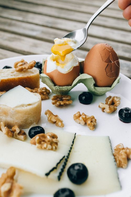 Free Delicious gourmet breakfast with soft-boiled eggs, cheese, nuts, and fruits on a rustic plate. Stock Photo