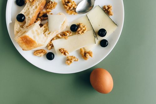 Free A stylish breakfast plate featuring cheese, walnuts, olives, and bread on a green background. Stock Photo