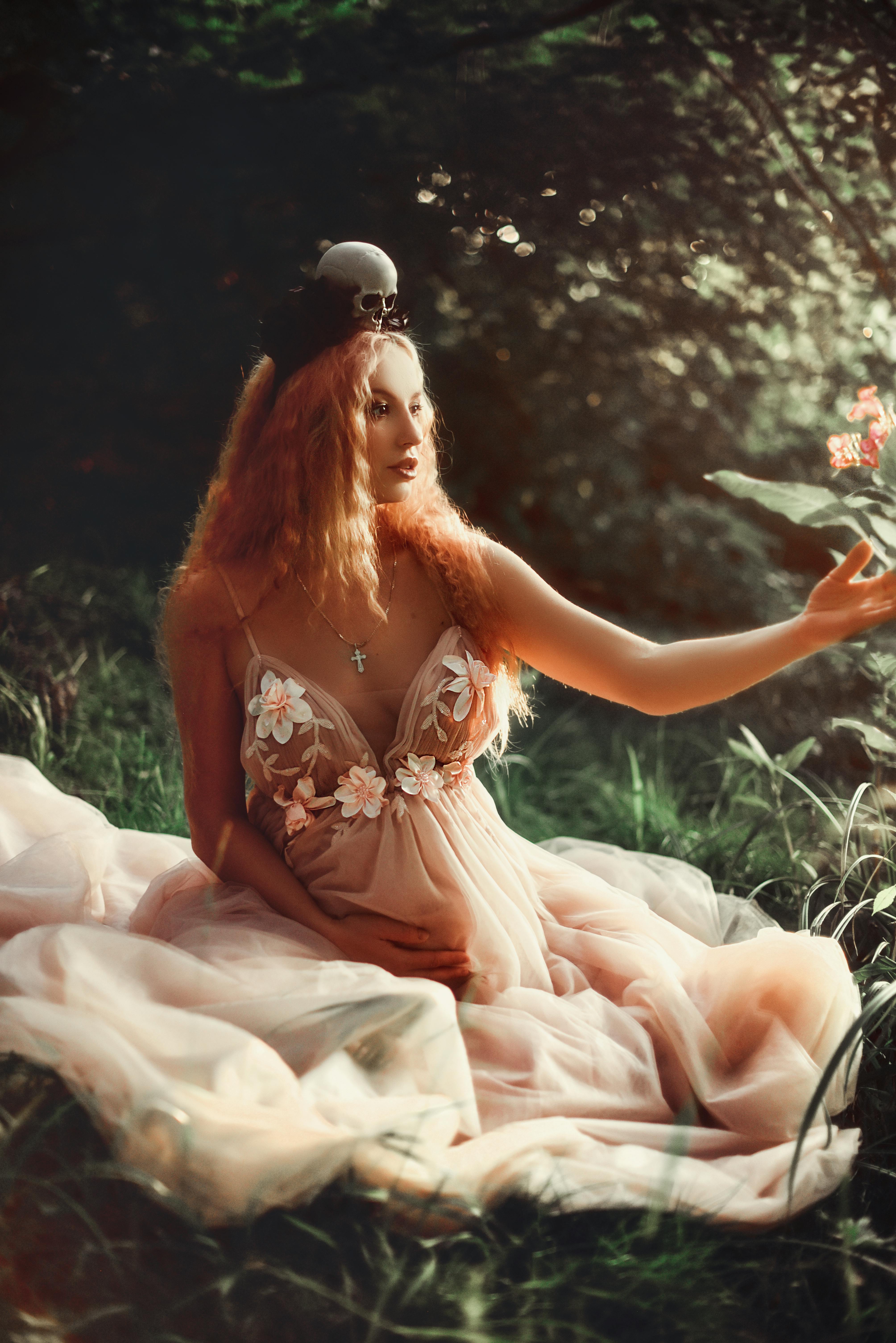 Delicate woman in a pink gown seated on lush green grass, exuding a dreamy and enchanted atmosphere.