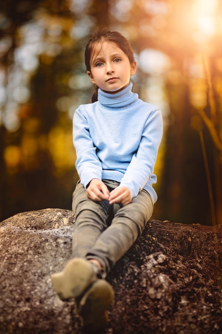 Calm Preteen Girl Sitting On Stone In Sunny Forest