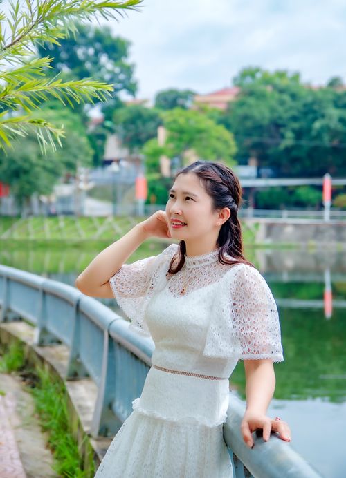 Free A young woman in a white dress enjoys a peaceful moment by the bridge, under lush greenery. Stock Photo