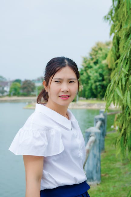 Portrait of an Asian woman in a white blouse standing by a riverside on a clear summer day.