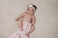 室内，一个戴着发带、裹着毯子的新生儿，正可爱地躺着，显得纯真又温暖