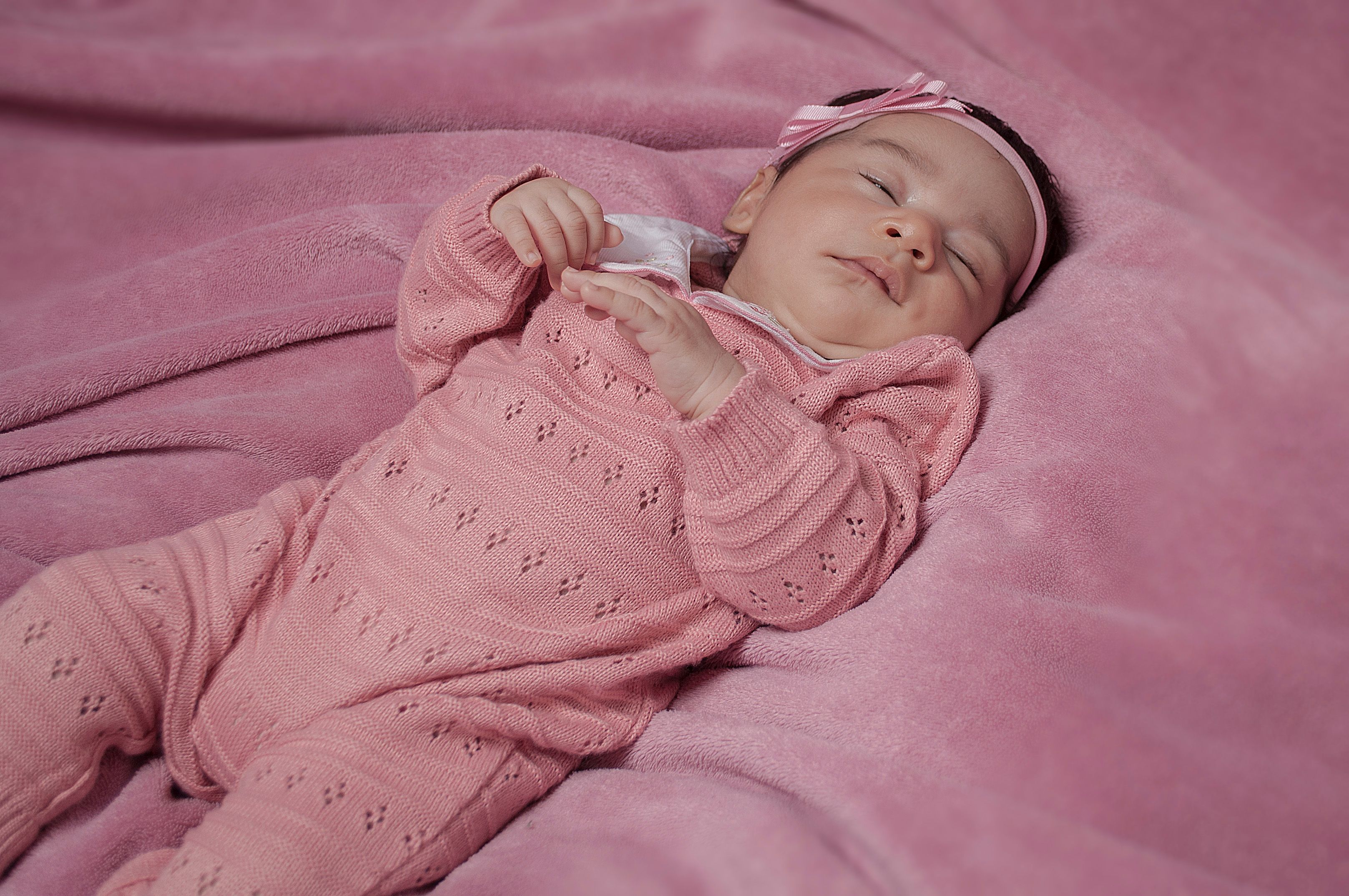 Bebê menina recém-nascida dormindo em cobertor rosa, vestida com tricô rosa