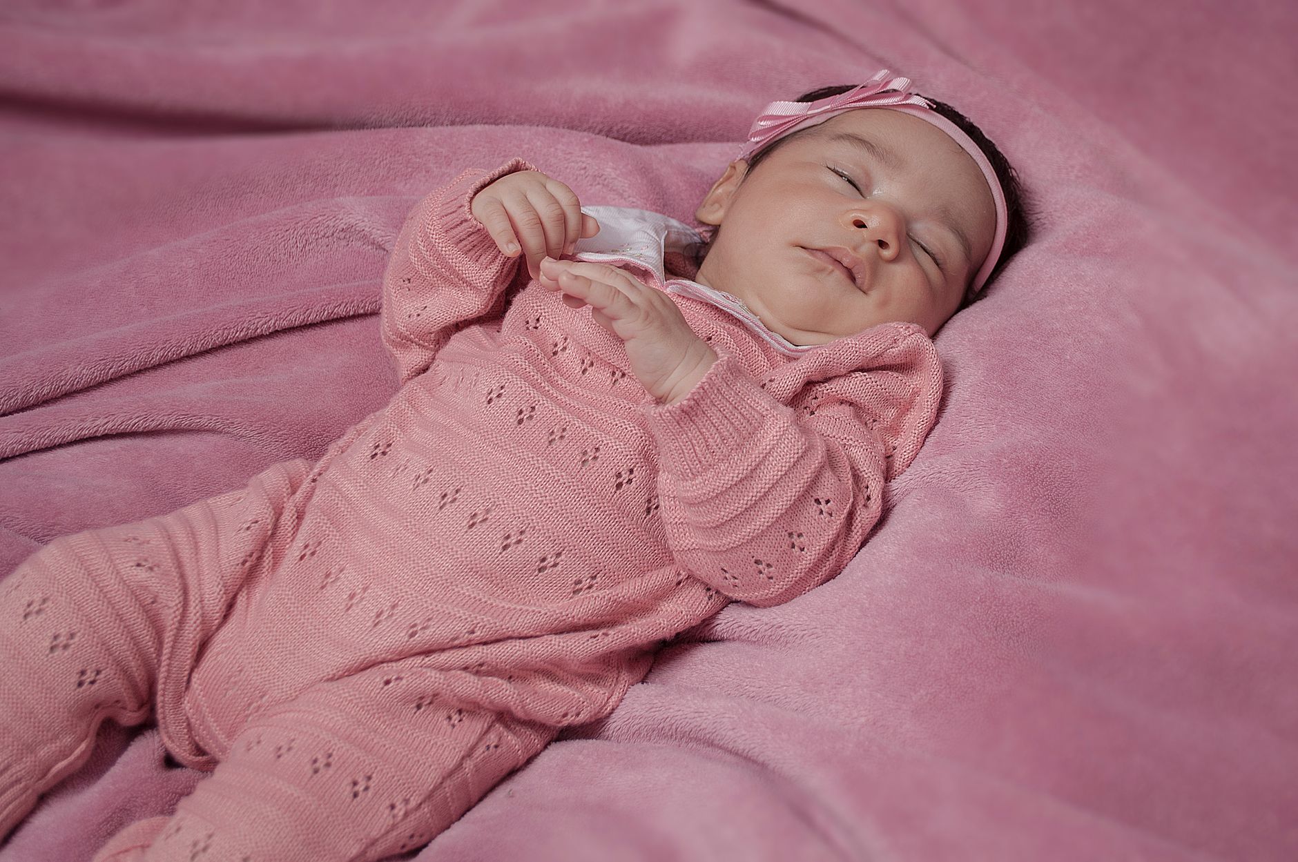 Bebê menina recém-nascida dormindo em cobertor rosa, vestida com tricô rosa