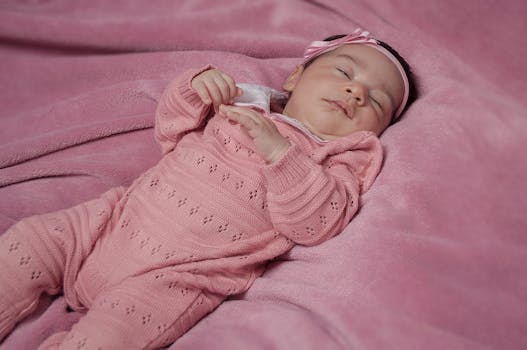一个穿着粉色针织衫的女婴安详地睡在舒适的粉色毯子上