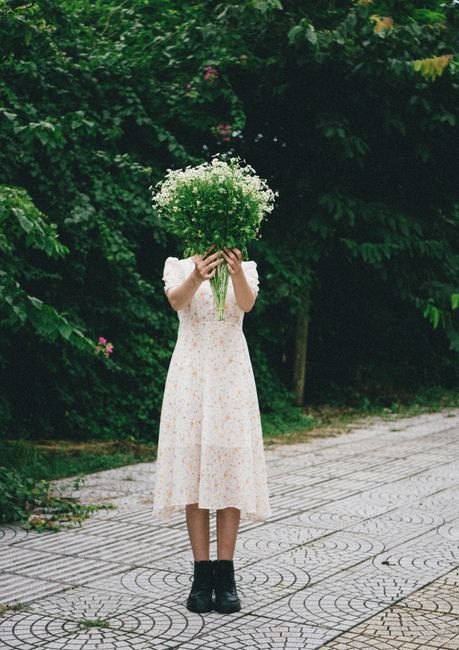 A girl in a white dress standing outdoors, holding a bouquet above her head.