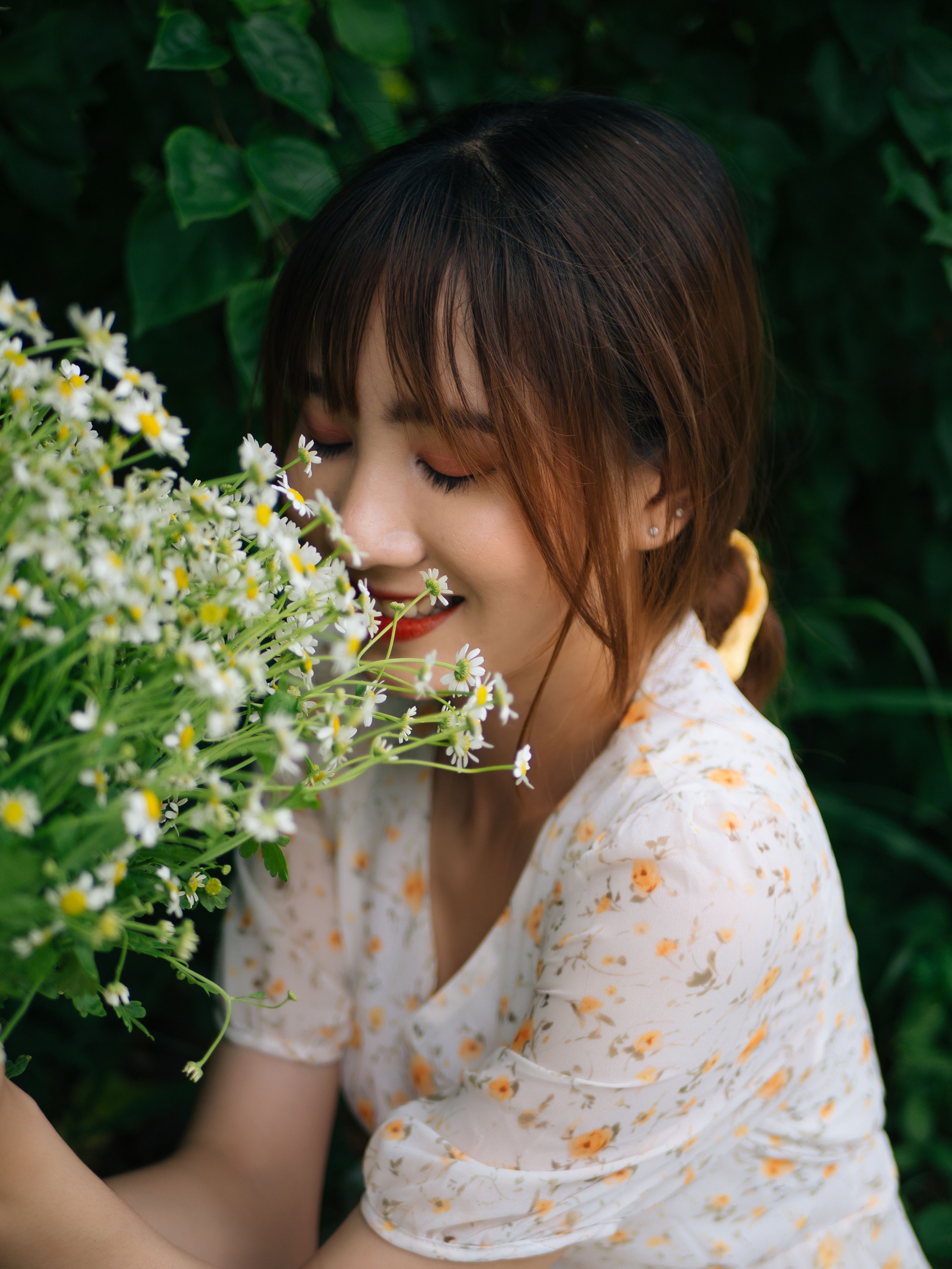 一位年轻女子闭着眼睛，在花园里微笑着享用新鲜的雏菊花束