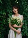 一位穿着夏装的年轻女性手捧鲜花，注视着镜头
