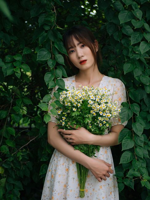 Young female in summer dress holding bouquet of fresh flowers and looking at camera