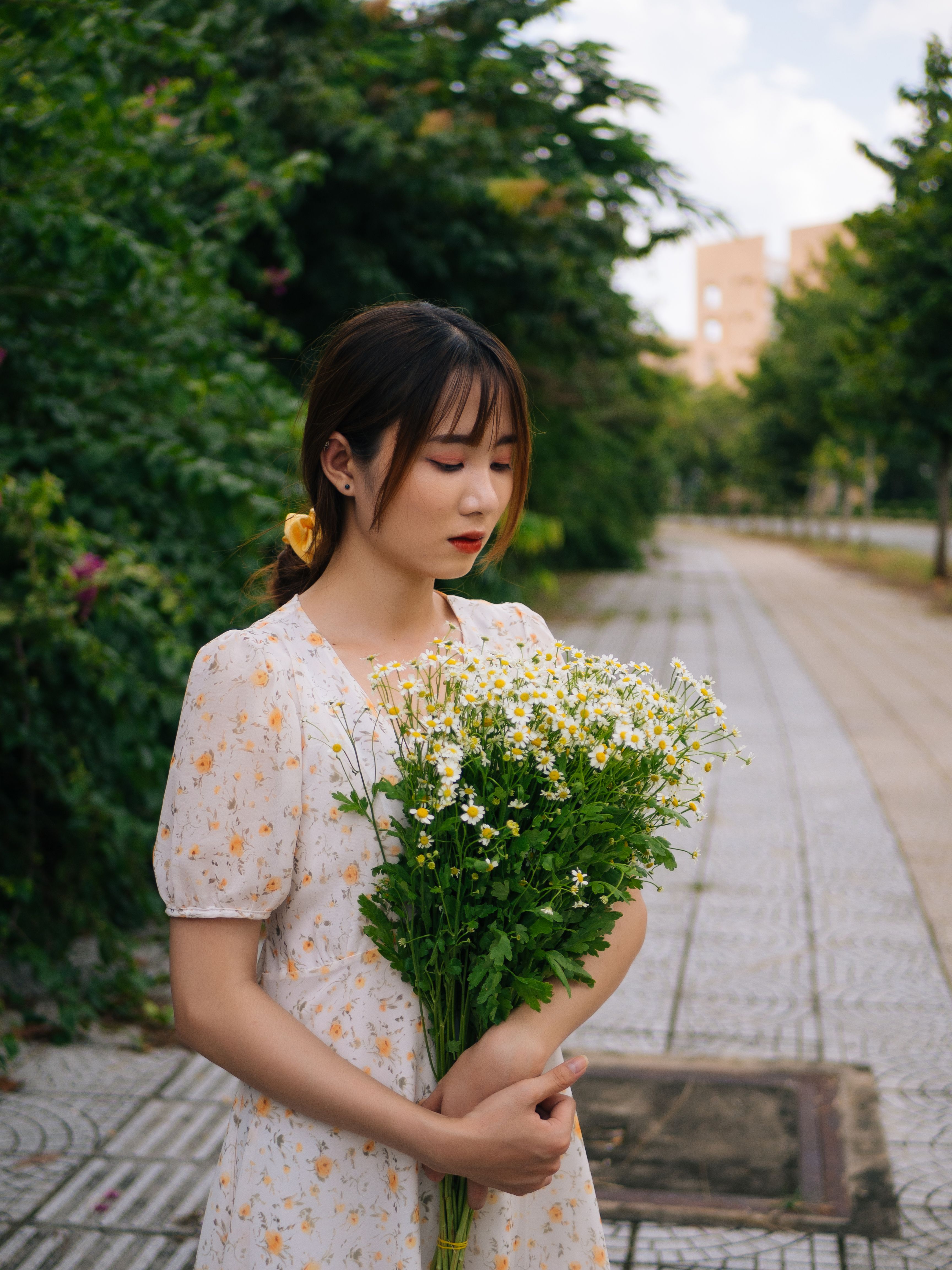 一位身着休闲装的年轻女性手拿鲜花，低头站在公园里