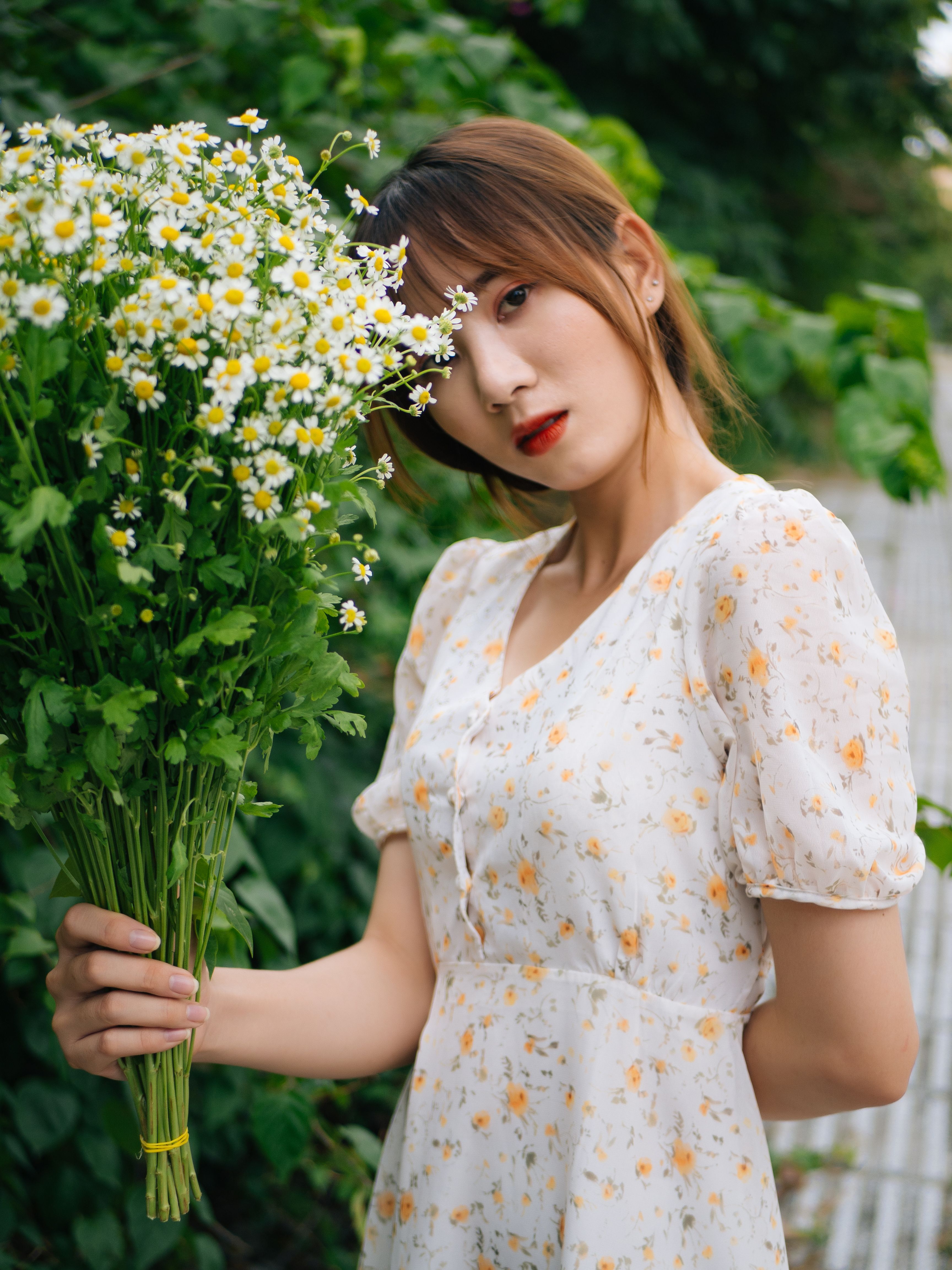 一位穿着夏装的时尚年轻女子在户外拿着一束雏菊