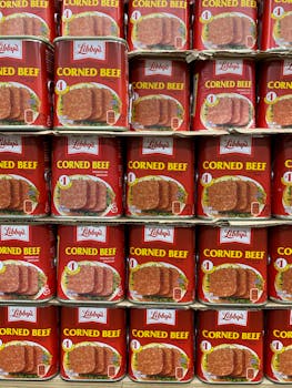 Multiple cans of corned beef neatly organized on supermarket shelves.