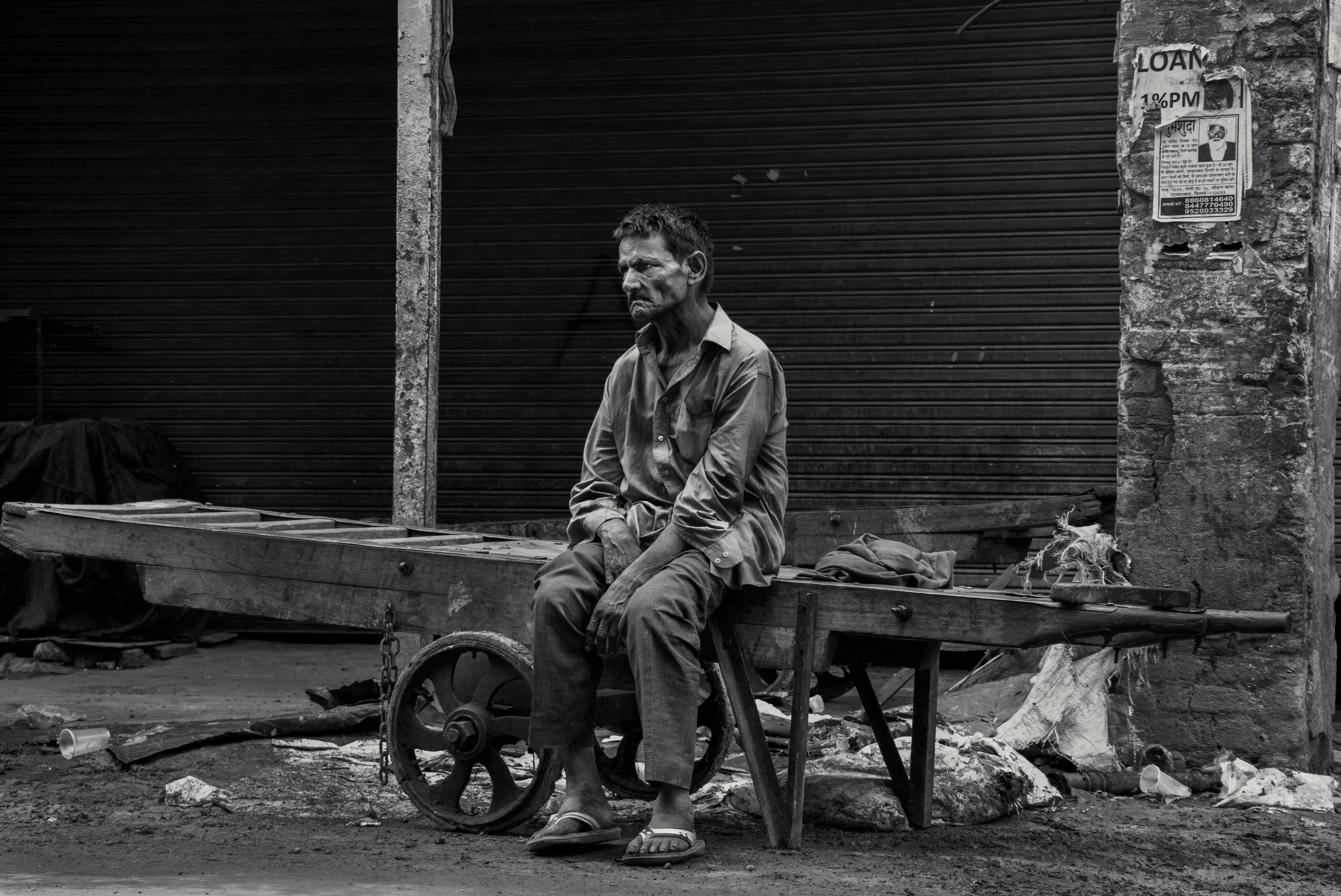 A man sits pensively on a cart, reflecting urban life's struggles.