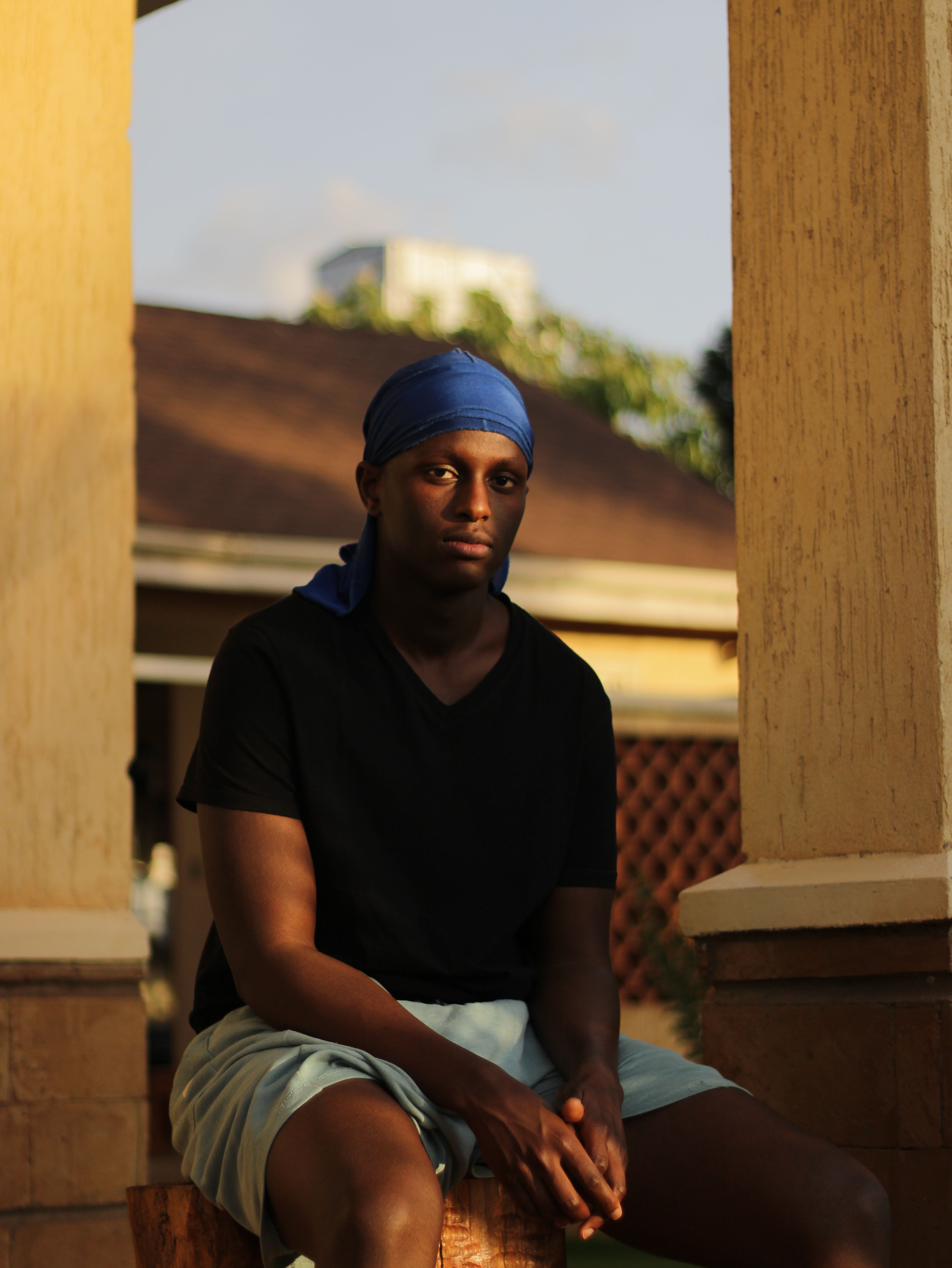 A serious man wearing a blue headband sits outdoors in the shade, captured in warm daylight.