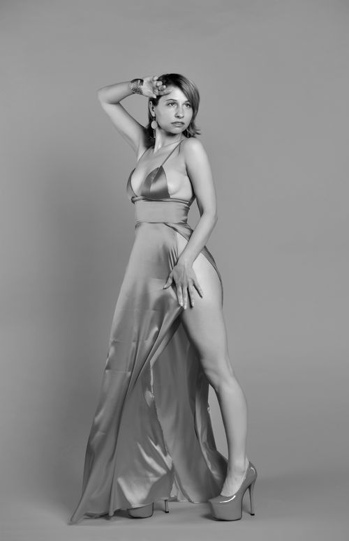 Free Full length of black and white young alluring lady in stylish dress with decollete and slit touching forehead and looking away Stock Photo