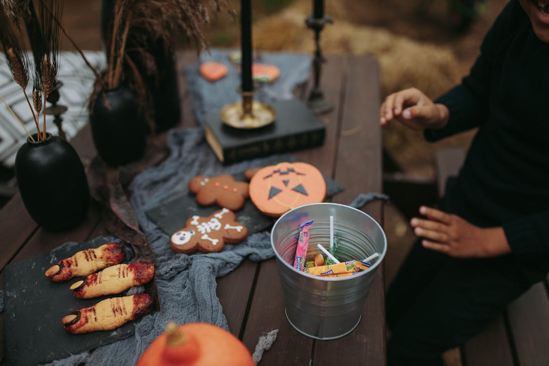 Free A Person Sitting at a Table with Halloween Decorations and a Bucket of Candies Stock Photo