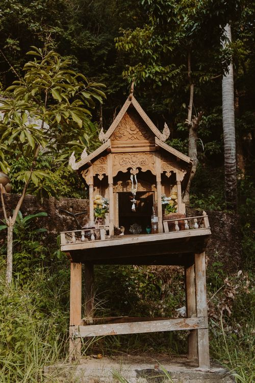 Free A beautifully crafted wooden spirit house surrounded by lush greenery in Thailand's serene forest. Stock Photo