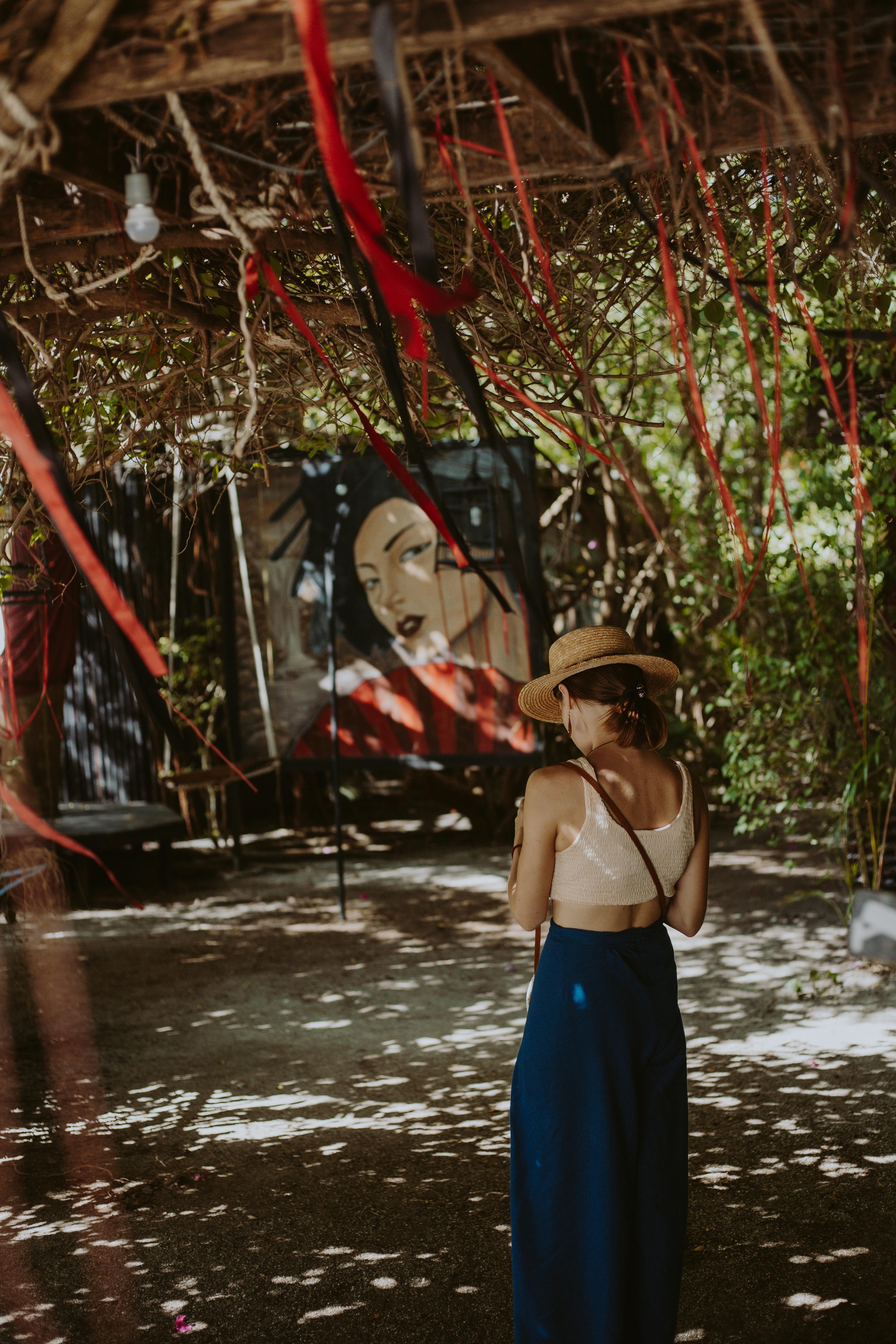 woman in blue spaghetti strap dress wearing brown straw hat standing under brown tree