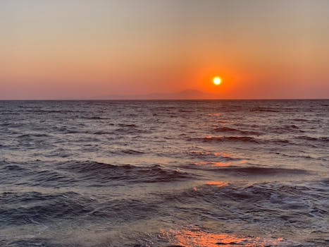 Breathtaking view of the ocean at sunset with a vibrant orange sky and gentle waves.