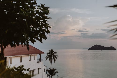 Free Serene coastal view with ocean, island, and tropical palm trees at sunset. Stock Photo