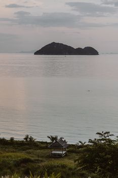 宁静的风景中，地平线上有一座小岛，日落时分，海边有一间小屋
