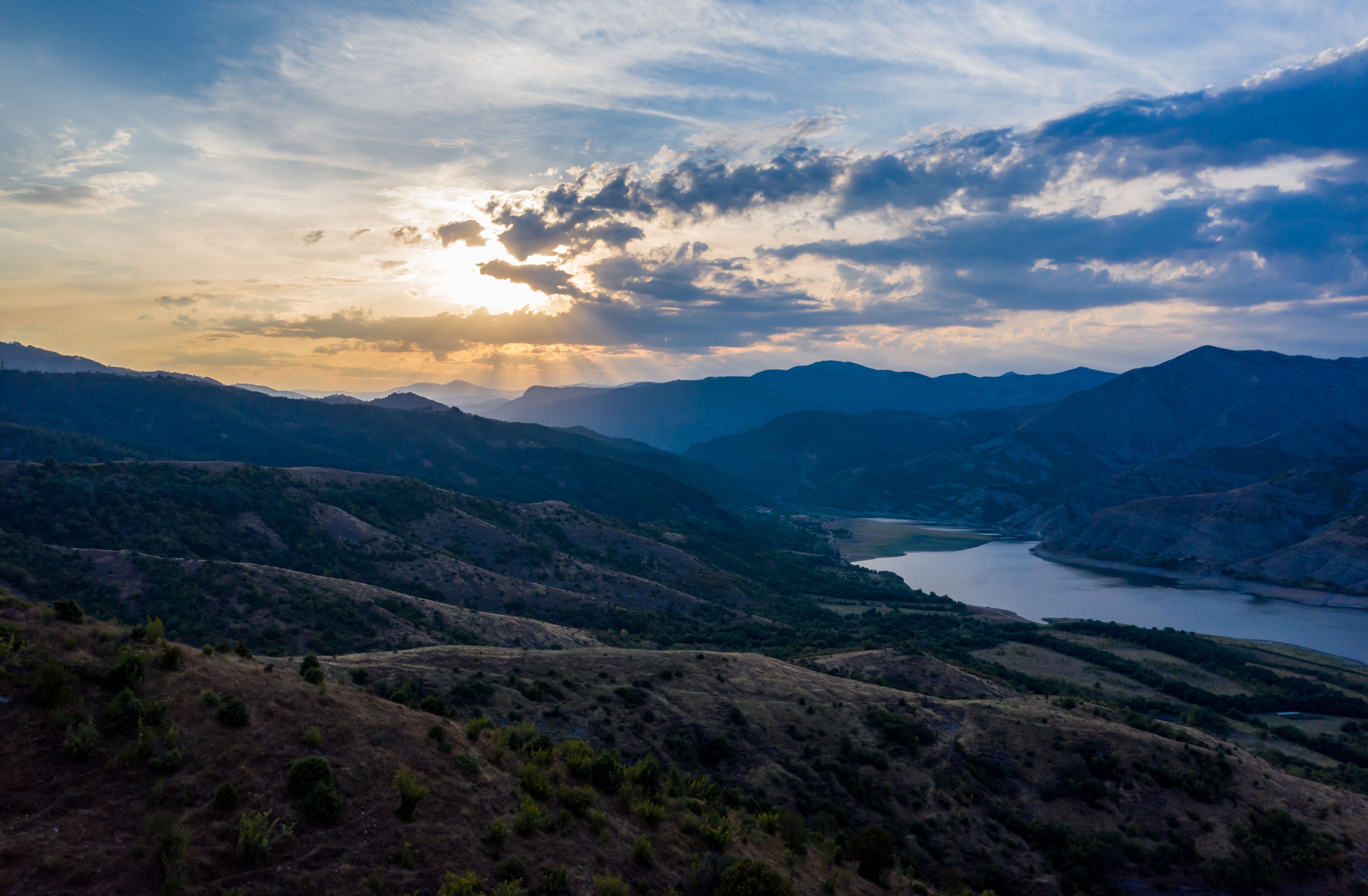 Stunning mountain landscape with sunrays breaking through clouds over a serene valley.