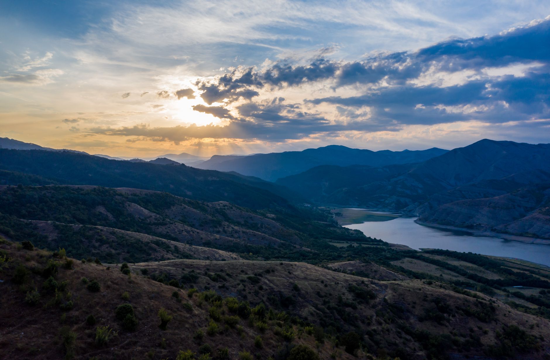 Stunning mountain landscape with sunrays breaking through clouds over a serene valley.