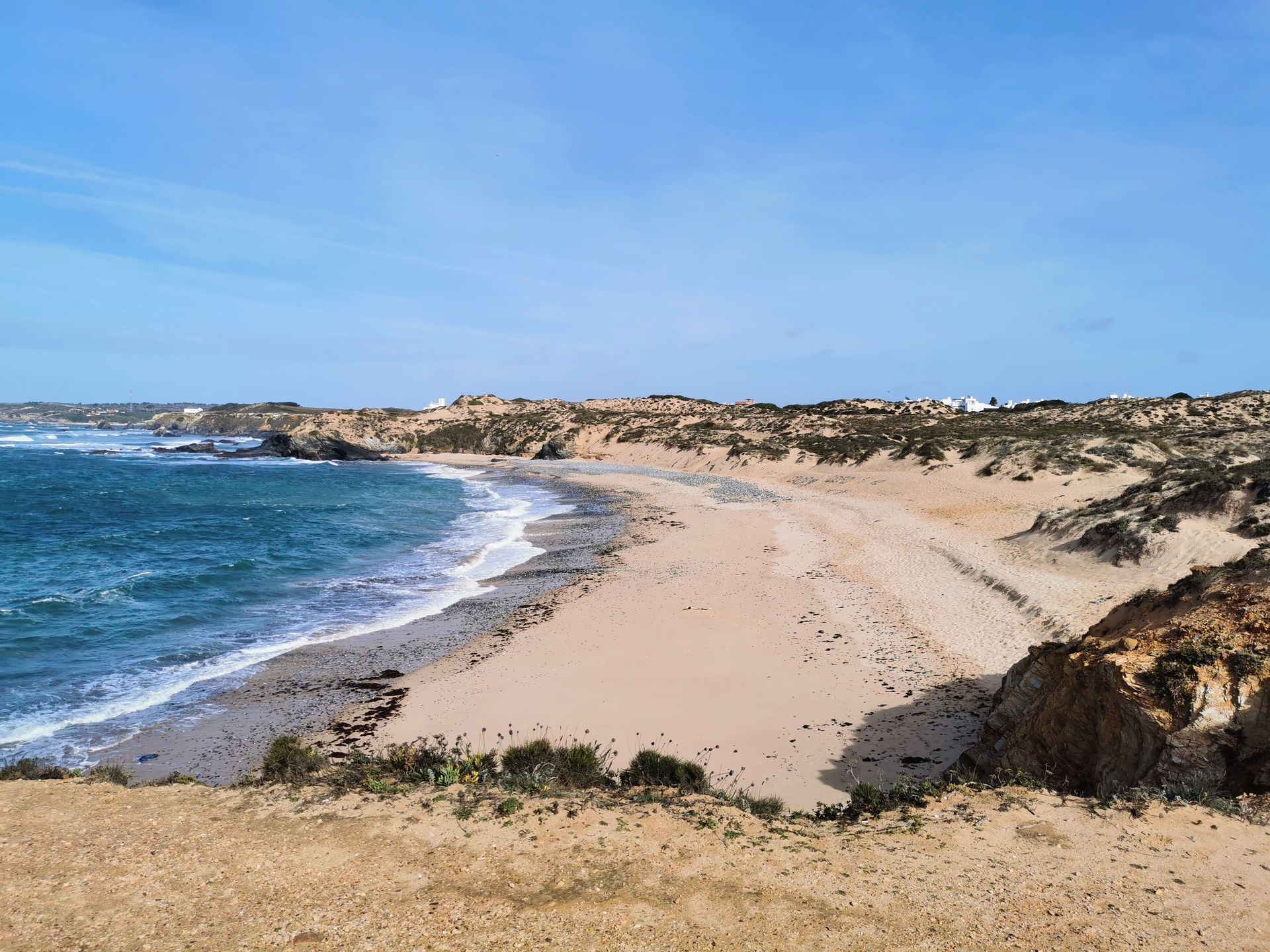 Explore the serene sandy beach and clear blue waters at Vila Nova de Milfontes, Portugal.