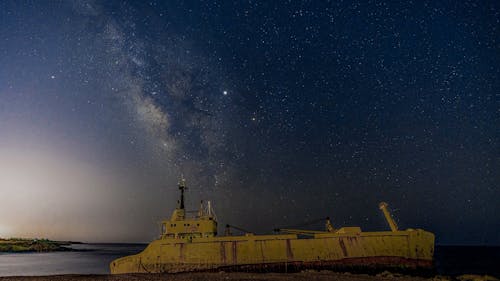 Old ship floating in ocean under sky with stars at night sky