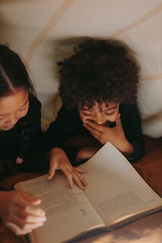 Two children enjoy reading a book together in a dimly lit, cozy tent setting.