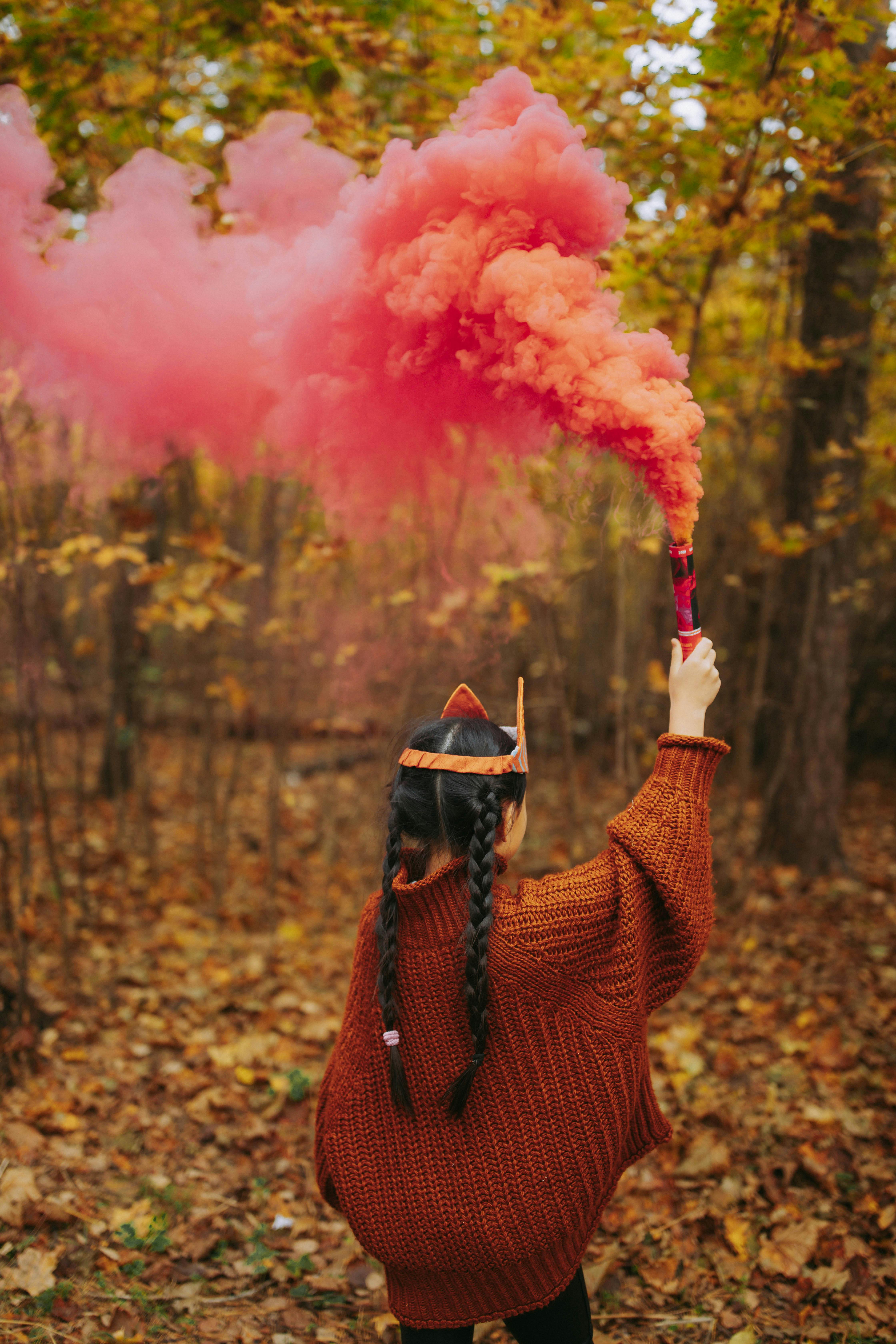 a back view of a young girl in brown knitted sweater holding a smoke bomb