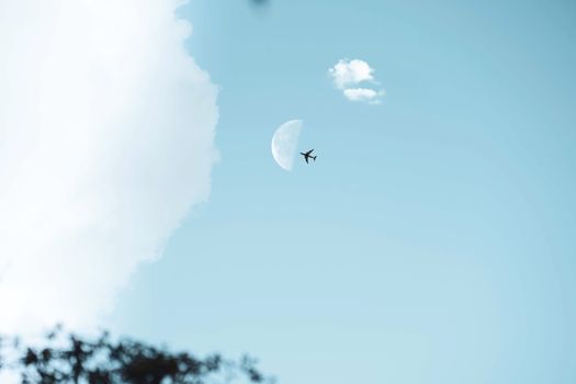 Aerial view of an airplane flying past a half-moon in a clear blue sky, capturing the essence of travel and adventure.
