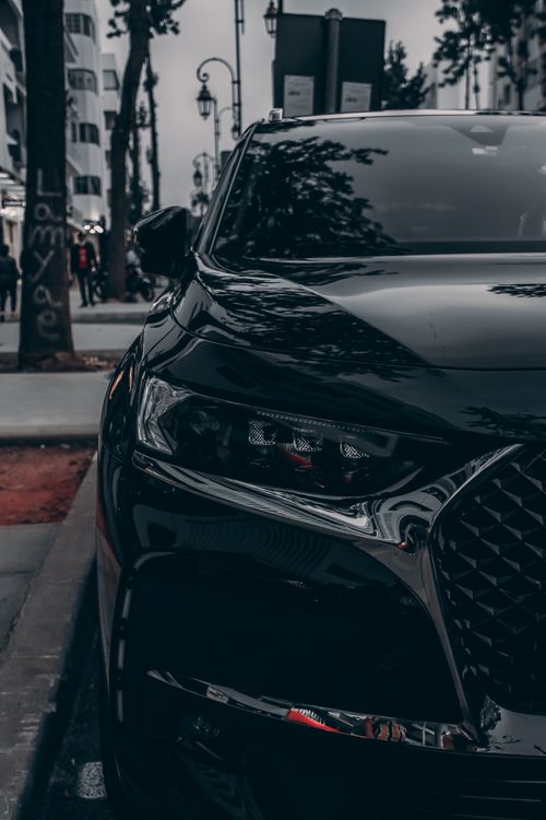 Free Close-up of a stylish black car parked on a Rabat sidewalk with cityscape reflections. Stock Photo