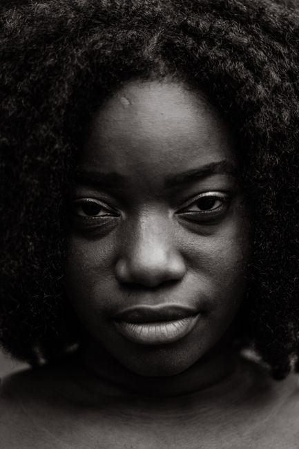 Black and white of crop attractive African American female with wavy hair intently looking at camera