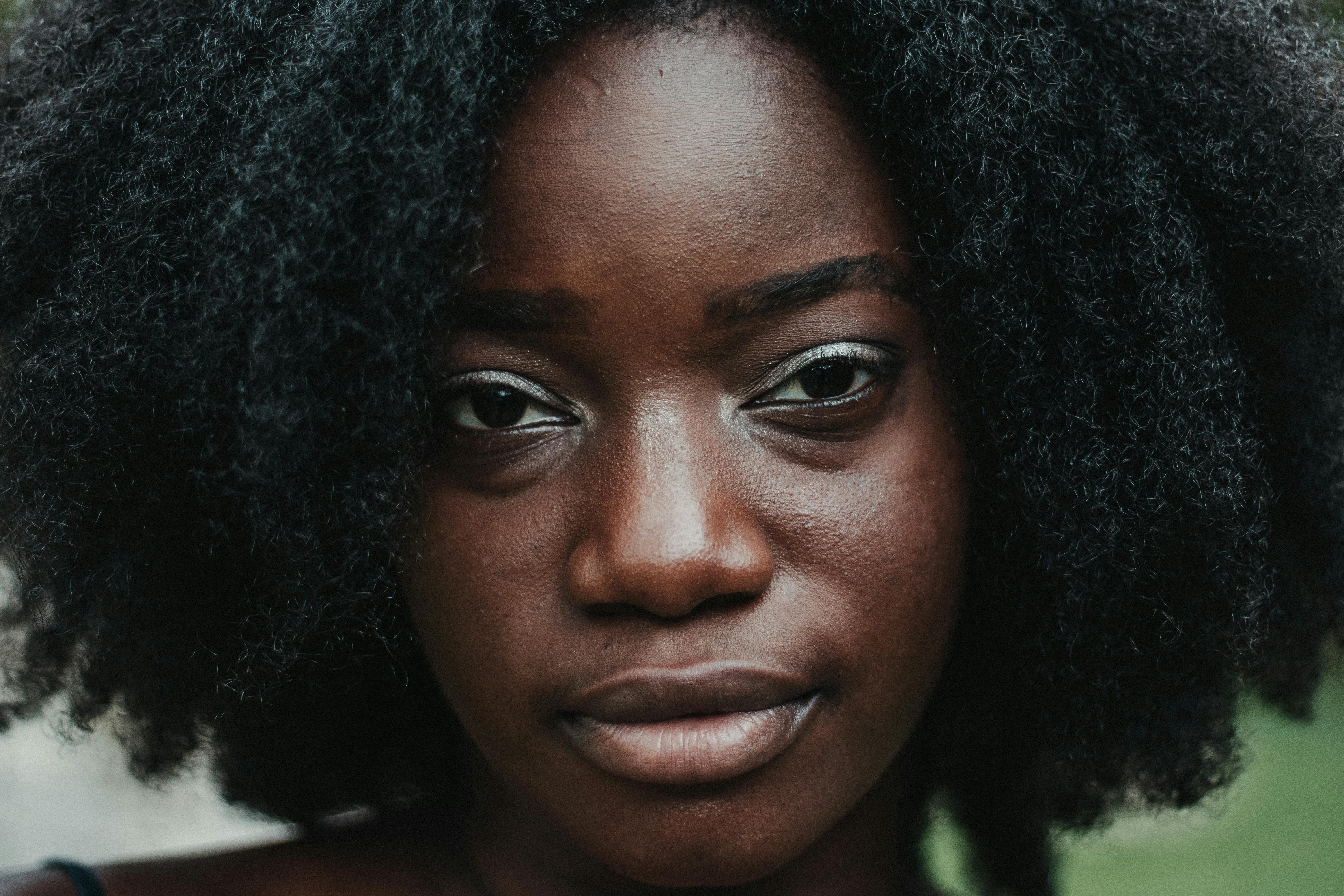 Pleasant black female with curly hair and perfect skin looking at camera on blurred background