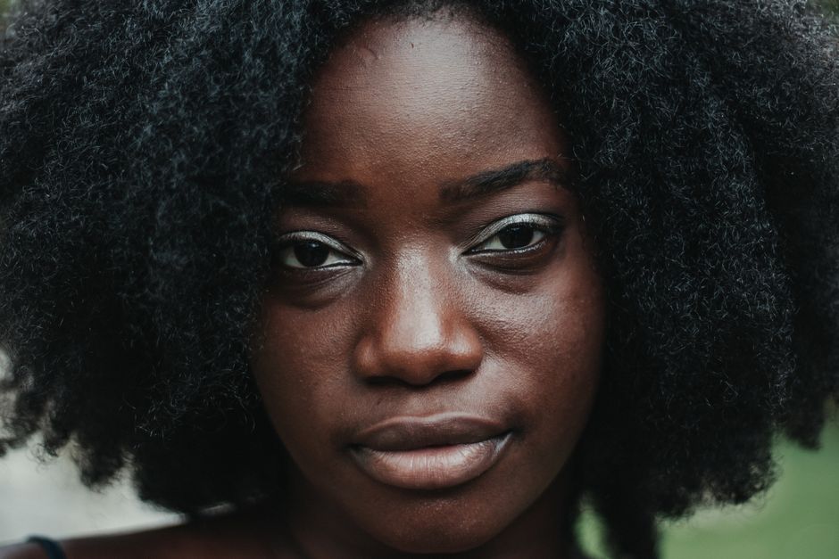 Pleasant black female with curly hair and perfect skin looking at camera on blurred background