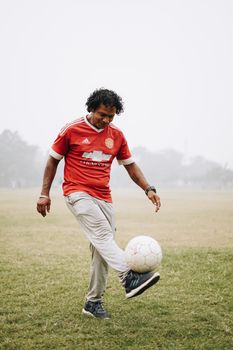 Full length of happy ethnic soccer player wearing t shirt and dirty pants hitting ball while training on football field
