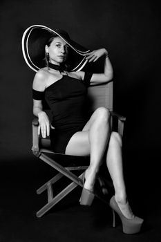 Full body of black and white young self assured lady in mini dress and hat sitting on chair in studio and looking away